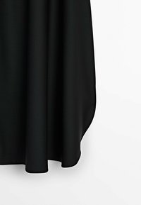 Jupe en tissu noir avec un ourlet arrondi tombant doucement sur un fond blanc.