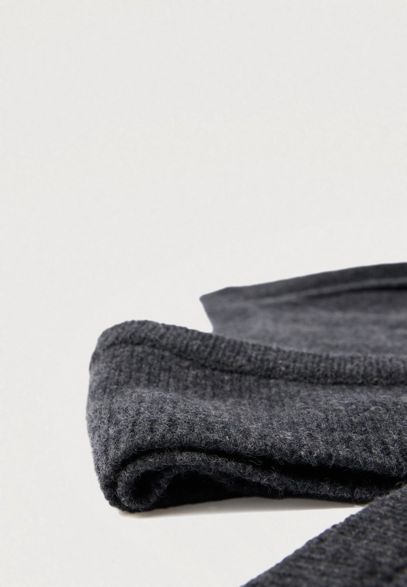 Tissu tricoté gris foncé plié avec une texture côtelée et des accents lisses, présentant des fibres douces et duveteuses à la surface.