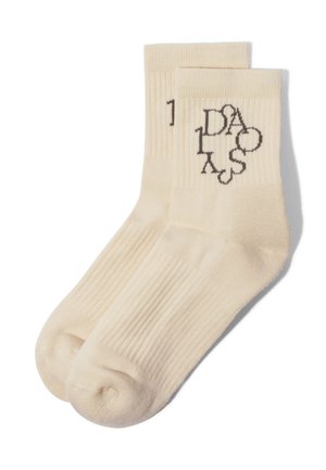 Kremowe, prążkowane skarpetki za kostkę z czarnym abstrakcyjnym napisem przy ściągaczu, ułożone płasko i nałożone na siebie na białym tle.