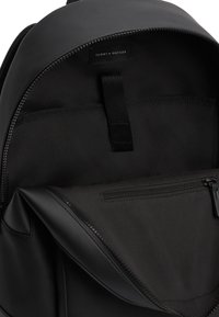 Μαύρο εσωτερικό σακιδίου με λεία υφή. Ορατή τσέπη με φερμουάρ και δύο υφασμάτινες θήκες. Ετικέτα εμπορικού σήματος στο πάνω μέρος, μινιμαλιστικός σχεδιασμός.