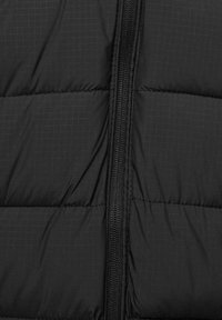 Tissu matelassé noir avec une fermeture éclair noire verticale au centre, coutures visibles sur les sections rembourrées.