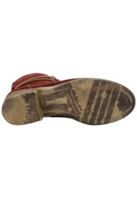 Botte en cuir rouge avec une semelle texturée, présentant des signes d'usure. Elle dispose d'une fermeture éclair latérale et d'un design de cheville courbé. La semelle a un grip à motif.