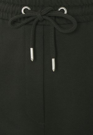 Gros plan sur un pantalon de survêtement noir à cordon de serrage avec embouts argentés, noué en nœud papillon à une taille élastique avec œillets métalliques.