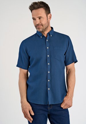 Korte mouwen blouse met knopen in donkerblauw, textuurbare stof met een borstzak en witte knopen. Draagt bij donkere jeans.