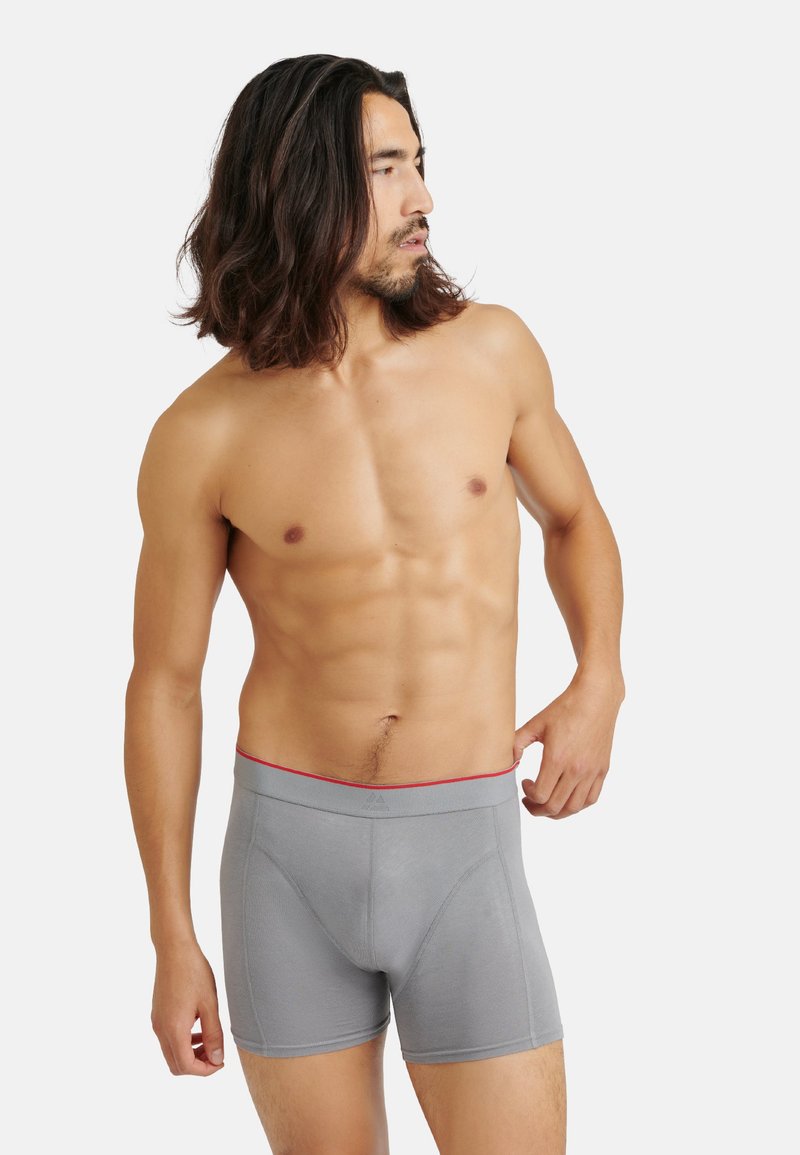 Boxer in grigio con elastico rosso, caratterizzati da un tessuto liscio e elasticizzato e un design aderente. Senza fantasie o dettagli aggiuntivi.