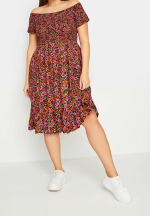 Kwiecista sukienka odsłaniająca ramiona z marszczoną górą, zdobiona różowymi, pomarańczowymi i zielonymi wzorami na czarnym tle; z falbanowanym dołem. Noszona z białymi tenisówkami.