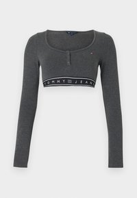 Γκρι cropped τοπ με μακριά μανίκια, στρογγυλή λαιμόκοψη, ραφή με κουμπιά και μαύρη ταινία με το κείμενο "TOMMY JEANS". Μαλακή υφή υφάσματος.