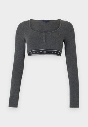 Γκρι cropped τοπ με μακριά μανίκια, στρογγυλή λαιμόκοψη, ραφή με κουμπιά και μαύρη ταινία με το κείμενο "TOMMY JEANS". Μαλακή υφή υφάσματος.
