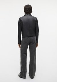 Schwarze Lederjacke mit kurzem Schnitt, kombiniert mit grauen Jeans aus Denim mit hohem Bund und weitem Bein. Glatte Textur mit minimaler Detailierung.