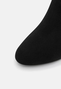 Bota negra de tobillo con punta afilada y textura de ante suave. Superficie lisa sin hardware ni ornamentación visibles.