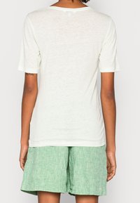 T-shirt verde chiaro a maniche corte con un taglio rilassato e scollatura ampia. Il tessuto è leggero e leggermente strutturato.