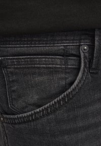 Jeans de denim negro con una textura suave, costuras visibles y un bolsillo delantero con un pequeño botón metálico.