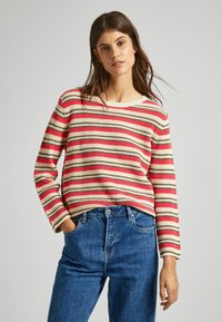 Maglione a righe in maglia con linee rosse, beige e marroni; scollatura rotonda; maniche lunghe; abbinato a jeans in denim blu.