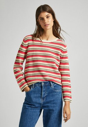 Maglione a righe in maglia con linee rosse, beige e marroni; scollatura rotonda; maniche lunghe; abbinato a jeans in denim blu.