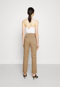Camisola bianca con schiena incrociata, abbinata a pantaloni beige su misura. Il modello indossa sandali neri con tacco. Stile minimalista.