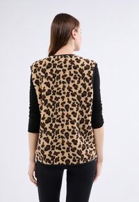Kamizelka w panterkę o miękkiej, puszystej fakturze. Czarno-brązowe plamy na beżowym tle. W połączeniu z czarną bluzką z długim rękawem i spodniami.