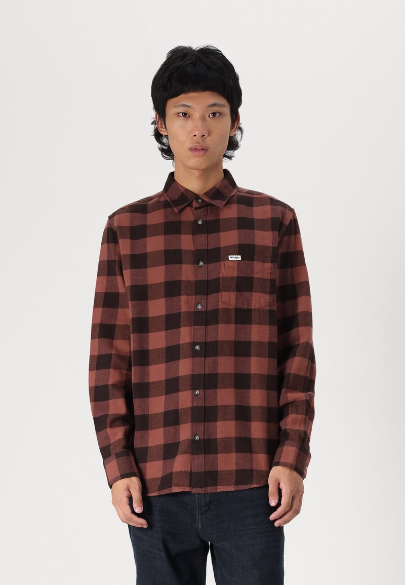 Camisa de cuadros en rojo y negro, con botones, hecha de franela, que presenta un bolsillo en el pecho, botones negros y mangas largas.