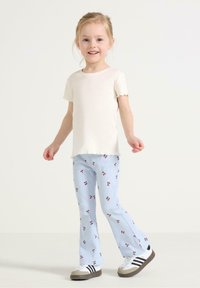Lys beige ribbet kortærmet t-shirt parret med blå stribede flagrende bukser med et kirsebærmønster. Hvide sneakers med sorte striber.