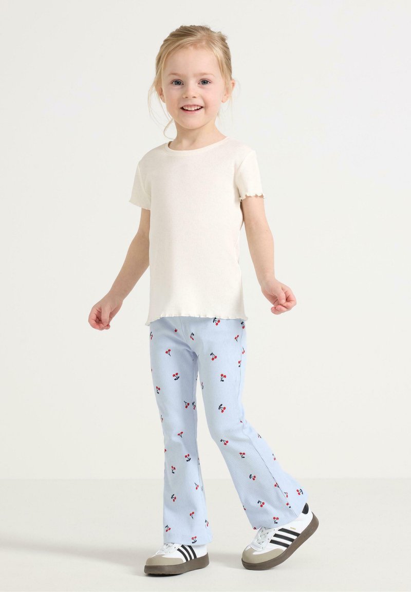 Lys beige ribbet kortærmet t-shirt parret med blå stribede flagrende bukser med et kirsebærmønster. Hvide sneakers med sorte striber.