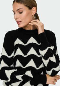 Maglione a zigzag bianco e nero con collo alto e polsini a coste, realizzato in un morbido materiale a maglia.