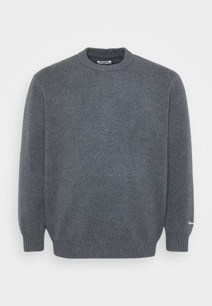 Tamsiai pilkas crew neck vilnonis megztinis su raukšlėmis ant rankovių ir apačios, paprasta mezginio tekstūra ir mažas baltas logotipo detalė ant kairiojo rankovės raukšlės.