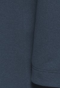 Tessuto di un blu navy scuro con una superficie liscia, caratterizzato da un motivo a coste. Mostra due sezioni del tessuto sovrapposte lungo il bordo.