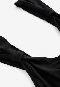 Top en tissu noir avec une texture douce, présentant un design de nœud tordu aux épaules et une silhouette simple et minimaliste.