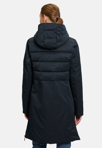 Zwarte pufferjas met capuchon, met een geborduurde bovenkant en een gladde onderkant. Lange mouwen en een rechte snit.