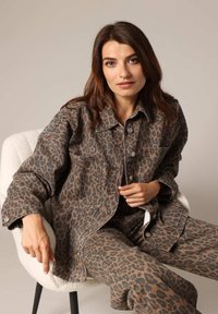 Veste en denim imprimée léopard avec une coupe surdimensionnée, fermetures à boutons et poches poitrine, associée à un pantalon assorti. Motif marron et noir.