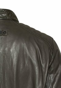Brun læderjakke med et quiltet skulderdesign, der har en tekstureret overflade og en subtil glans. Inkluderer en detalje med en sort lædermærke.