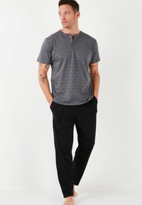 Camisa Henley gris de manga corta con un patrón sutil, combinada con pantalones negros que tienen dos bolsillos laterales y un ajuste relajado.