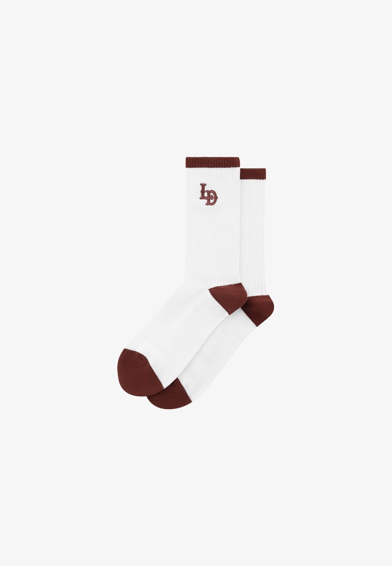 Sosete din bumbac alb cu textură ribbed, accent maro la vârf și la manșetă, având un mic logo maro. Perechea este prezentată stivuită.