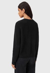 Maglione nero lavorato a maglia con una vestibilità rilassata, scollo rotondo e polsini a coste. Tessuto morbido, visto da dietro, abbinato a jeans scuri.