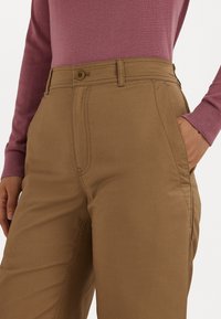 Beige bikses ar pogu aizdari, sānu kabatām un redzamām šuvēm. Pāris ar gaiši purpura garām piedurknēm.