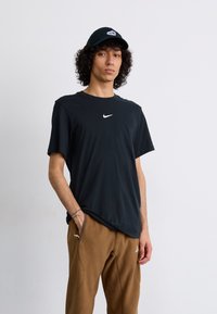 Black Nike t-shirt with a white swoosh logo, short sleeves, relaxed fit. Brown fleece pants with pockets, subtle stitching detail.