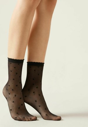 Svarta ankelsockor gjorda av genomskinligt material, med ett mönster av små svarta hjärtan och en scalloped toppkant.