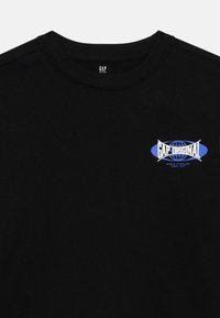 Black cotton t-shirt with a crew neck. Features a blue and white "GAP Original" logo on the chest within an oval design. Soft texture.