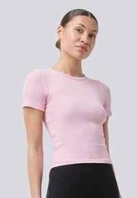 Rosa, gerippte Kurzarm-T-Shirt mit rundem Ausschnitt, taillierter Form und glatter Textur, kombiniert mit schwarzen Unterteilen.