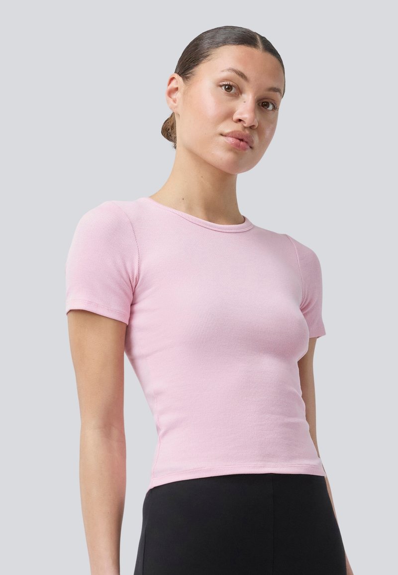 Rosa, gerippte Kurzarm-T-Shirt mit rundem Ausschnitt, taillierter Form und glatter Textur, kombiniert mit schwarzen Unterteilen.