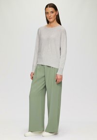 Lichtgrijze trui met een geribbelde textuur, gecombineerd met mintgroene broeken met een wijde pijp. De outfit heeft een ontspannen pasvorm en een eenvoudig ontwerp.