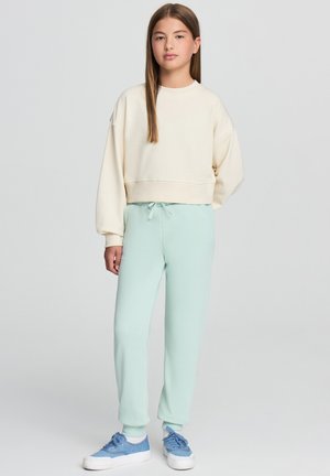 Pullover accorciato di colore crema con maniche ampie abbinato a pantaloni della tuta verde menta e sneakers blu. Tessuto morbido e vita elasticizzata.