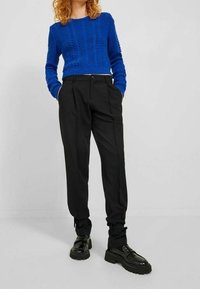 Blauwe gebreide trui met gestructureerd patroon, gecombineerd met zwarte op maat gemaakte broek en stevige zwarte schoenen. Effen kleuren en aansluitend ontwerp.