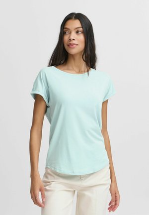 T-shirt bleu clair à manches courtes, fabriqué en tissu doux, avec un col rond et des manches retroussées, associé à un pantalon couleur crème.