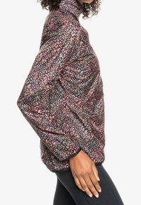 Veste matelassée noire avec un motif floral rose et violet, dotée d'un col haut et de manches longues. Le matériau semble texturé.