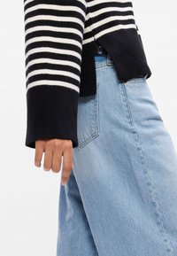 Sweater às riscas preto e branco com mangas largas, combinado com jeans de denim azul claro com um corte relaxado e detalhe na costura lateral.