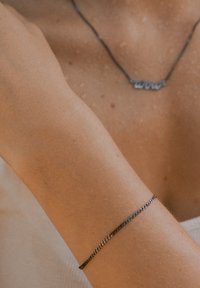 Silver chain bracelet on a light brown arm, part of a close-up. The bracelet features a delicate, interwoven design and smooth texture.