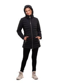 Chaqueta acolchada negra con cuello alto y cierre de cremallera, que cuenta con bolsillos laterales y capucha. Combinada con leggings negros y botas beige.