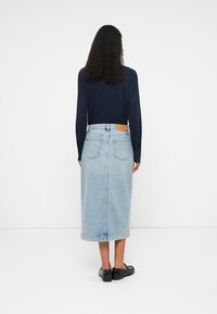 Saia de ganga azul-claro com corte reto, bolsos traseiros e um patch de couro castanho na cintura. Combinada com uma camisa de manga longa azul-marinho.
