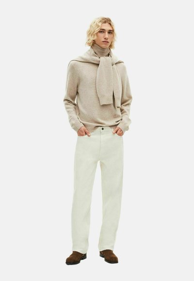 Maglione beige con una sciarpa avvolgente, abbinato a pantaloni bianchi dritti e scarpe in suede marrone. Design semplice e minimalista, texture morbida.