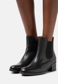 Botas de tobillo de cuero negro con paneles elásticos en los laterales, punteras redondeadas y un pequeño tacón cuadrado, que ofrecen un acabado liso y brillante.